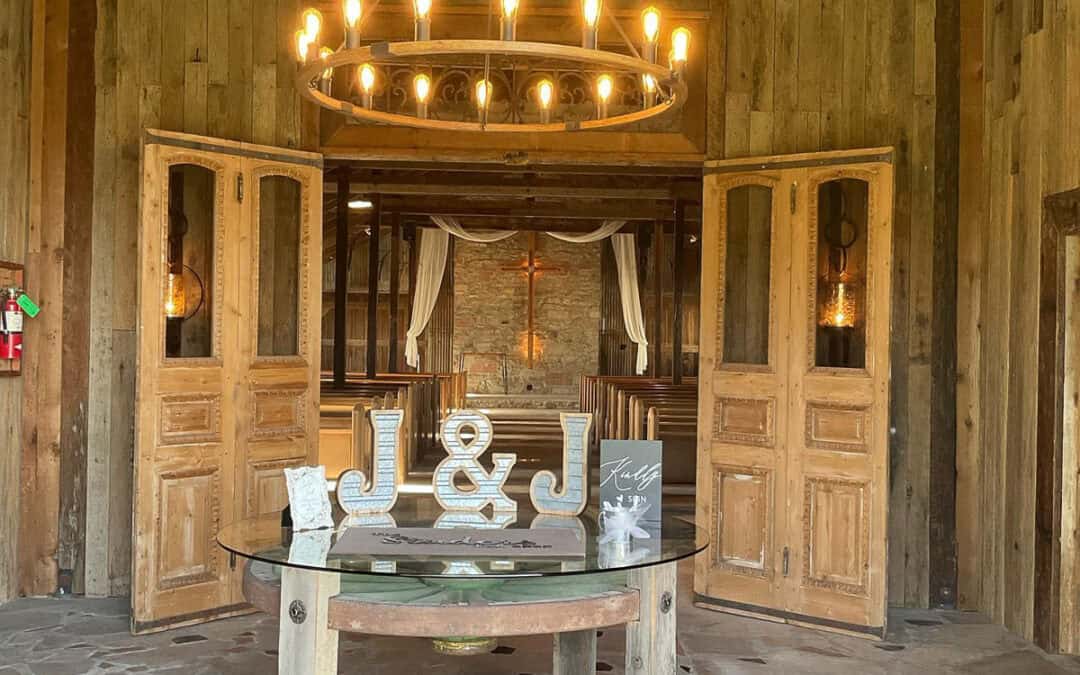 Rustic wedding venue with a wooden interior, a chandelier, and a glass-topped table with decorative letters J and J in the foreground.