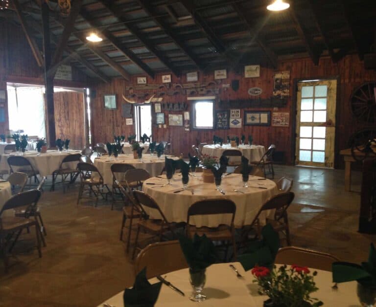 A rustic event venue with wood walls and ceiling, decorated tables set with green napkins, framed pictures, and memorabilia.