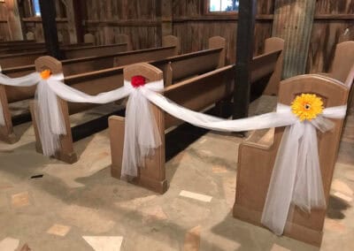 Church pews decorated with white tulle and yellow and red flowers for a wedding ceremony.