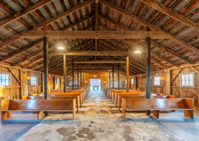 Rustic wood chapel interior with wood pews, a stone floor, and an open beam ceiling, lit by natural and artificial light.