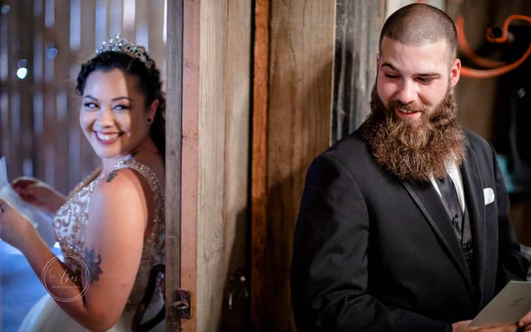 A bride and groom stand back-to-back on either side of a wooden door, smiling and holding notes.